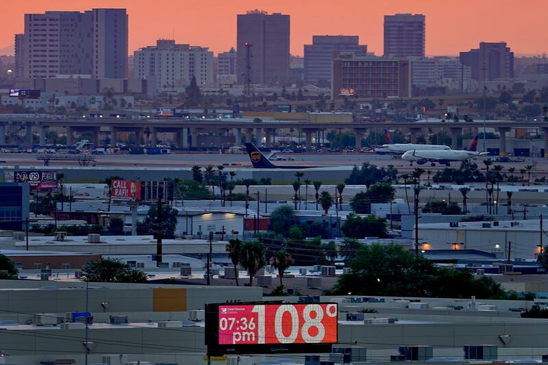 A sign displays an unofficial temperature of 108 degrees as jets taxi at Sky Harbor International Airport at dusk in Phoenix.