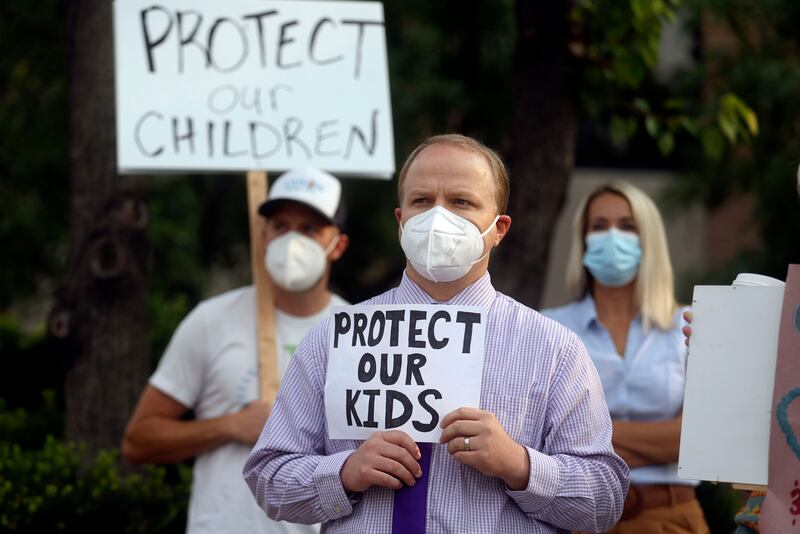 A man holds a sign supporting school mask mandates.