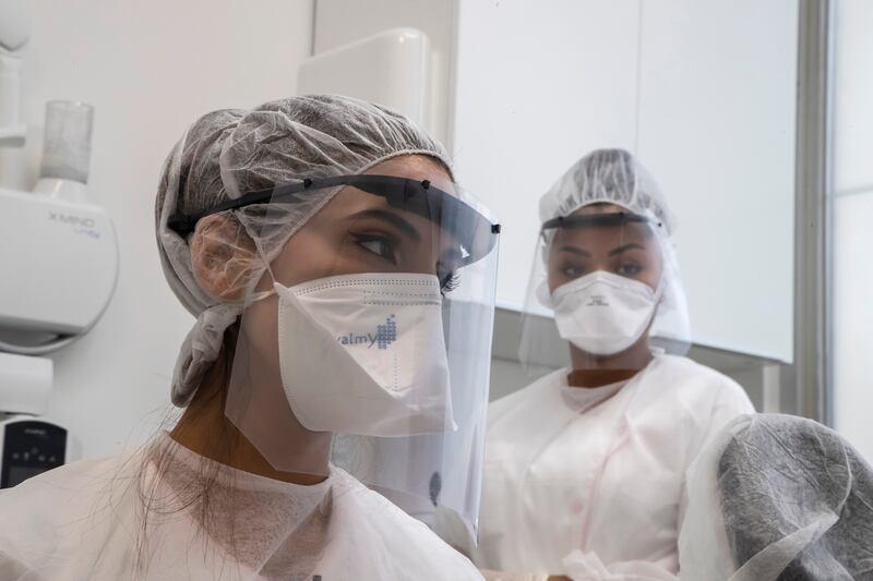 In this Wednesday, May 13, 2020 photo, dentist Sabrine Jendoubi, left, and her assistant Margot Daussat listen to a patient during a dental appointment, at a dental office in Paris.