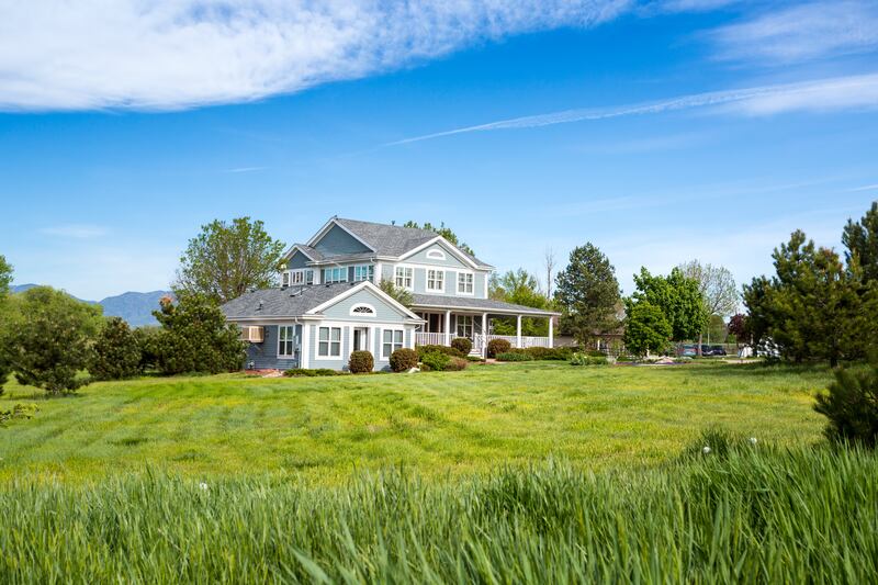 A large blue and white-trim house with a grassy green field in front on a sunny day.