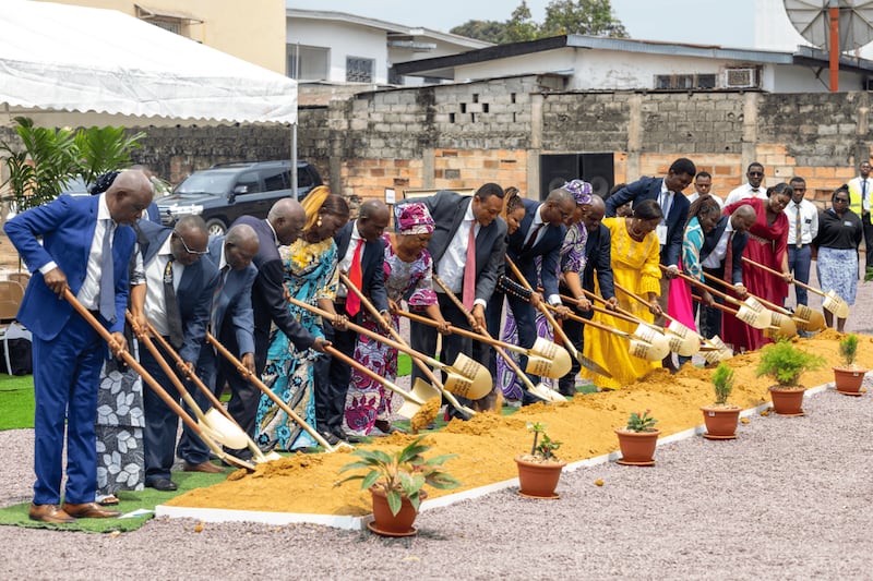 A line of people in Sunday best holding ceremonial golden shovels into the dirt.