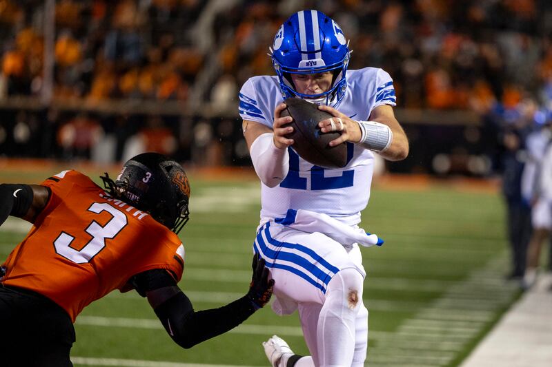 BYU quarterback Jake Retzlaff (12) jumps past Oklahoma State cornerback Cam Smith (3) for a touchdown in overtime of an NCAA college football game Saturday, Nov. 25, 2023, in Stillwater, Okla.