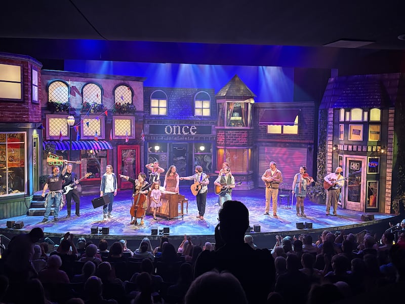 Ryan Boam, far left, holds up a guitar with the words "For Glen" taped on the back in honor of Irish singer-songwriter Glen Hansard, who died on July 29 at the age of 56. Boam stars in CenterPoint Theatre's production of "Once," which features Hansard's music.