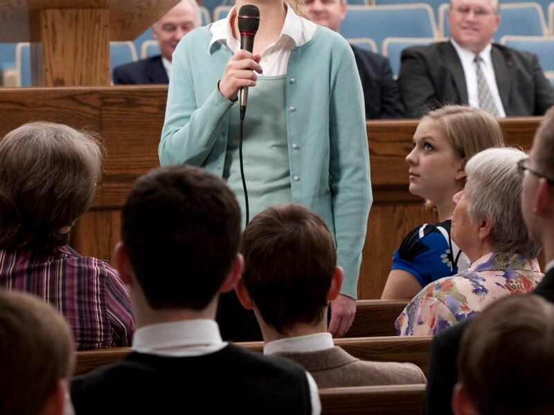 A woman stand and bears her testimony during sacrament meeting.