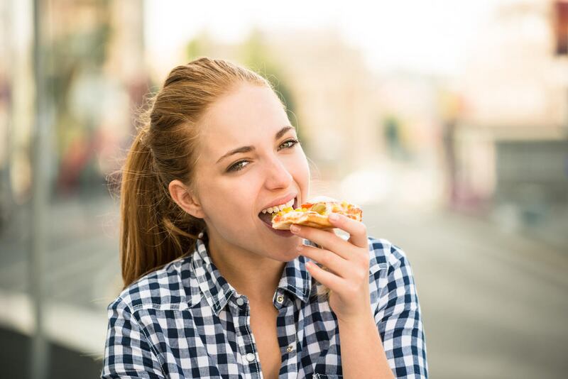 Teenager lifestyle - young woman eating pizza outdoor in street