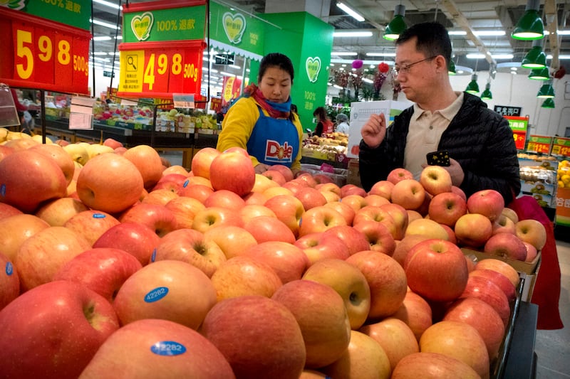 FILE - In this March 23, 2018, file photo, a woman wearing a uniform with the logo of an American produce company helps a customer shop for apples a supermarket in Beijing. China raised import duties on a $3 billion list of U.S. pork, fruit and other prod