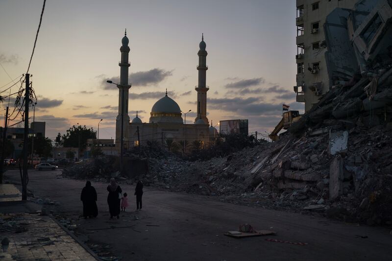 Palestinians walk next to the rubble of a building destroyed by an airstrike during an 11-day war between Gaza’s Hamas rulers and Israel, in Gaza City, Thursday, June 10, 2021.