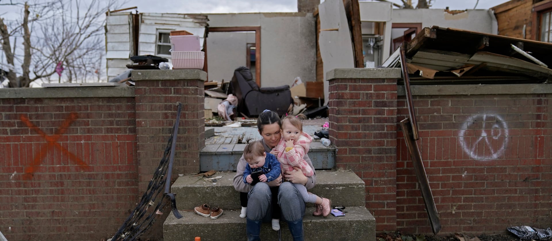 Halyn McKnight sits with her niece and a child of a friend as she searches for possessions from her destroyed home after tornadoes.