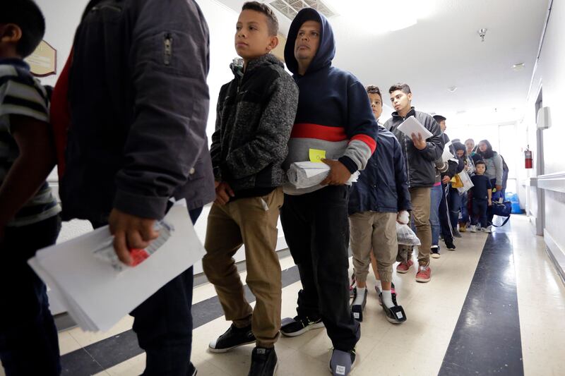 In this Friday, Jan. 11, 2019, photos, a line of migrants recently released by U.S. immigration authorities waits to check in at the Catholic Charities shelter in McAllen, Texas.