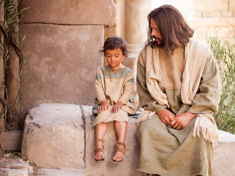 Jesus Christ sits with a young child while teaching that we must “become as little children” in this image from the Bible Videos series.