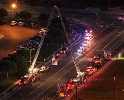 The processional passes an American flag hanging trom ladder trucks as the casket of Draper Battalion Chief Matt Burchett leaves the Roland R. Wright Air National Guard Base in Salt Lake City on Wednesday, Aug. 15, 2018. Burchett was killed while fighting