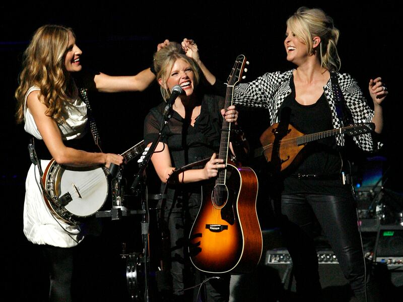 In this Oct. 18, 2007 file photo, Emily Robison, left, and Martie Maguire, right, adjust Natalie Maines’ hair as the Dixie Chicks perform at the new Nokia Theatre in Los Angeles.