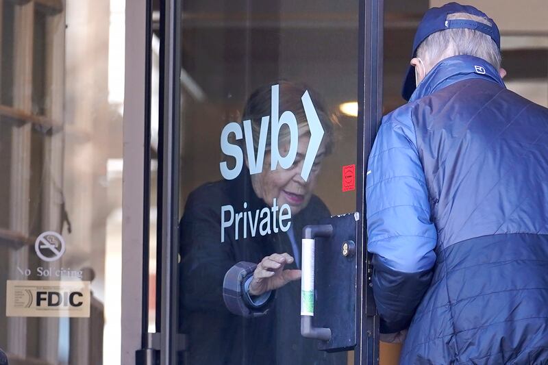 People enter and depart a Silicon Valley Bank branch location through a glass door, in Wellesley, Mass.