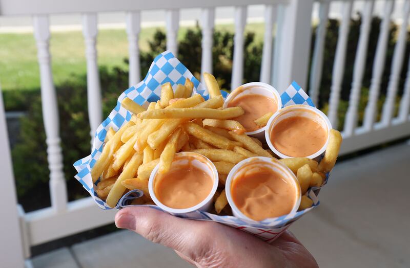 A man holds fries and fry sauce on the porch of a home.