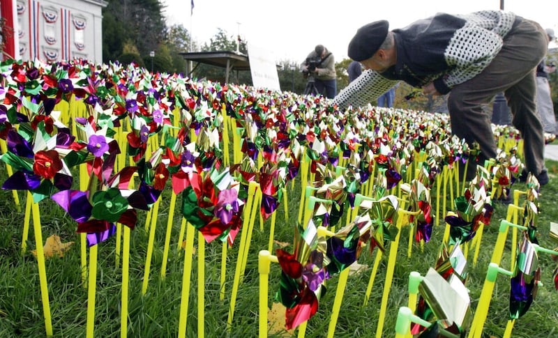 Lawrence Mott of Earth Turbines Inc. places some of almost 1,400 pinwheels on the Statehouse lawn