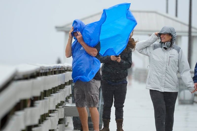 Three people walk through a storm while an umbrella blows in their face.