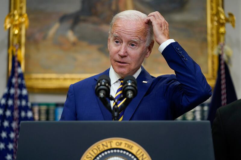 President Joe Biden stands at a podium and speaks with scratching his head.