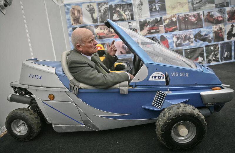 In a photo taken on March 24, 2009, Justin Capra, a Romanian inventor who claimed he beat the Americans to make the world’s first jet-pack, seen on photo wall behind top left, gestures sitting in a fuel efficient vehicle he designed at an inventions fair