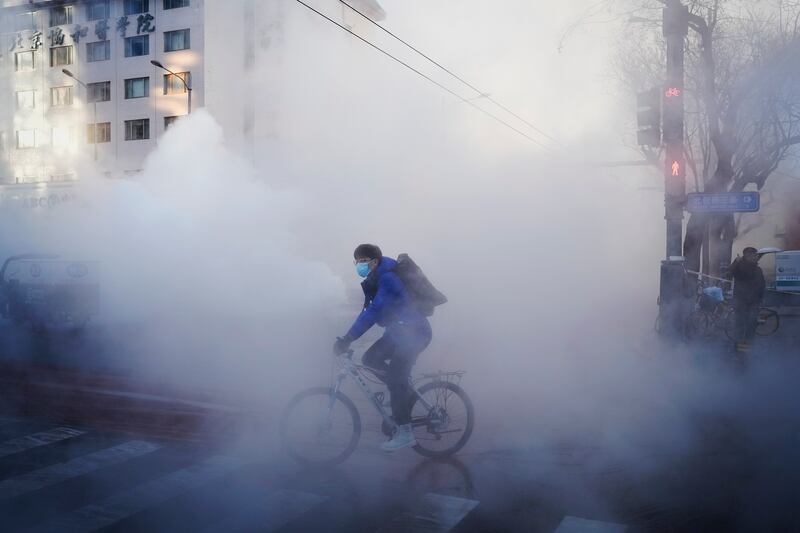 A cyclist rides through the steam leak of the water heating network in Dongcheng district during the morning rush hour in Beijing, Friday, Dec. 22, 2023. Temperatures has plunged across northern China, with a cold front moving eastward from Xinjiang in the west.