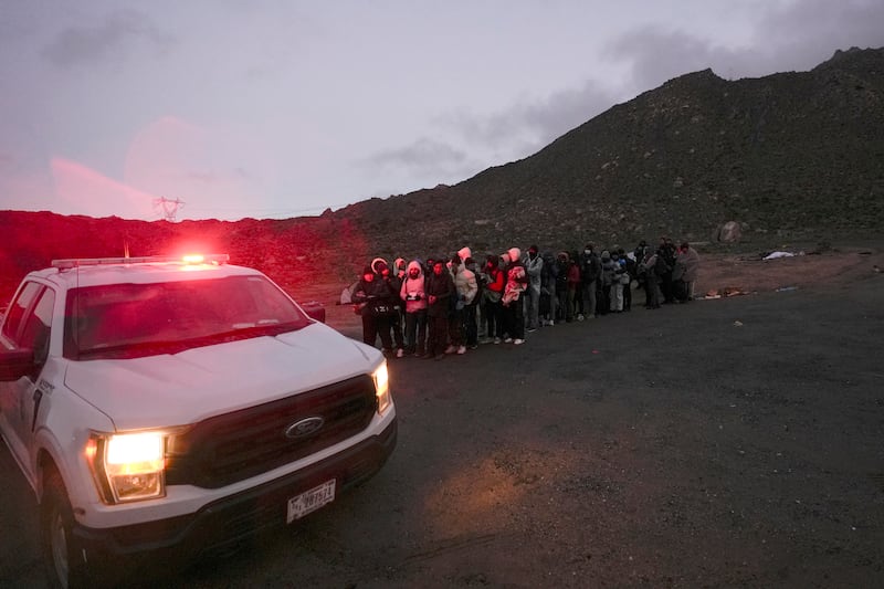 A group of asylum-seeking migrants line up to be processed after crossing the border with Mexico on Feb. 2, 2024, near Jacumba Hot Springs, Calif.