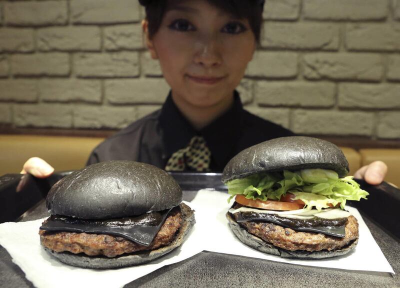 FILE - In this Sept. 16, 2014 file photo, Burger King employee Rumi Sekine shows the Kuro Diamond burger, right, and the Kuro Pearl burger at its Shibuya restaurant in Tokyo. The fast-food chain is offering customers an initially unappetizing experience a