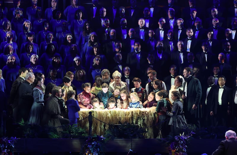Child and adult actors and singers look upon a lit manger during the 2023 concert “Christmas with the Tabernacle Choir.”