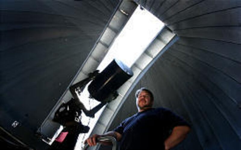 Wayne Springer, associate professor of physics, stands with a 12-inch optical telescope on the roof of the South Physics Building at the U. The school plans to install a larger telescope in southern Utah.
