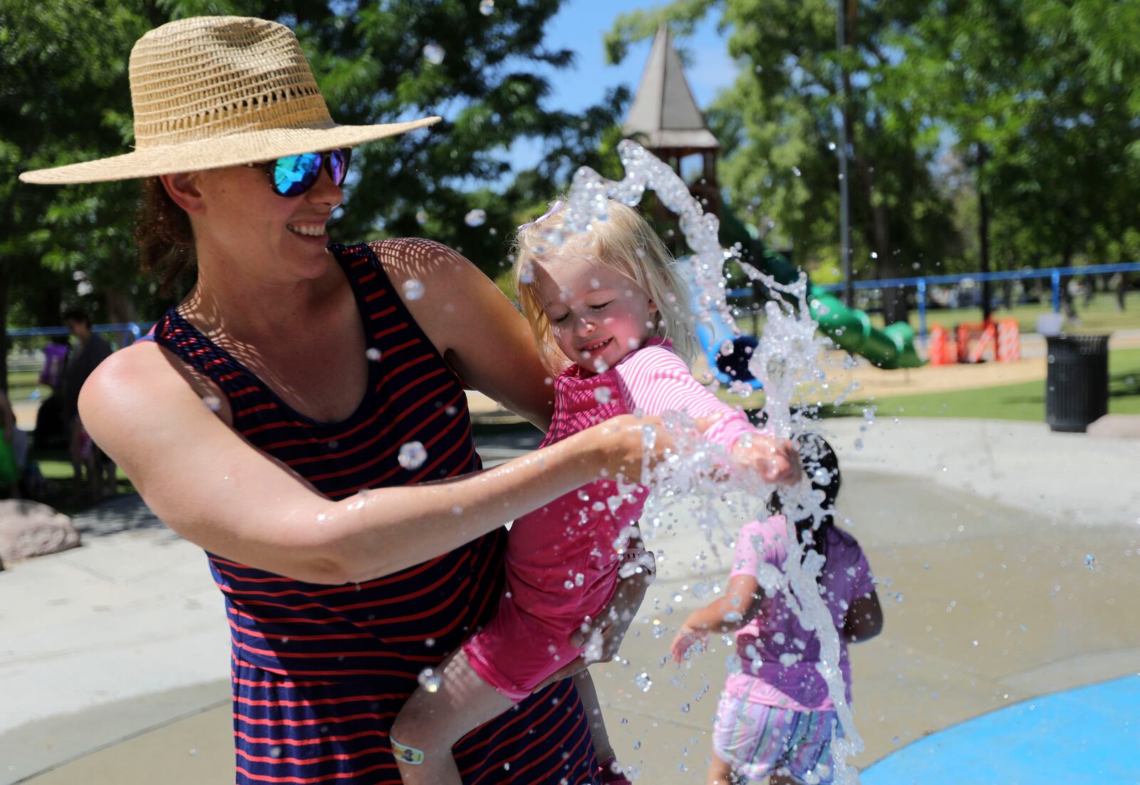 Kika Chelaru holds Bowie Walker as she tests out the water in the splash pad at Liberty Park during heat wave.