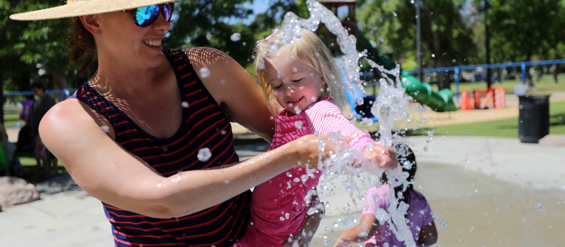 Kika Chelaru holds Bowie Walker as she tests out the water in the splash pad at Liberty Park during heat wave.