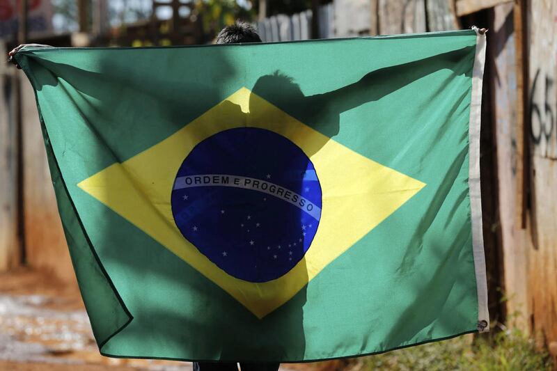 A boy walks with a representation of a Brazilian national flag through the Santa Luzia favela, ahead of fellow residents in a protest against the money spent on preparations for the upcoming World Cup, in Brasilia, Brazil, Friday, May 30, 2014.