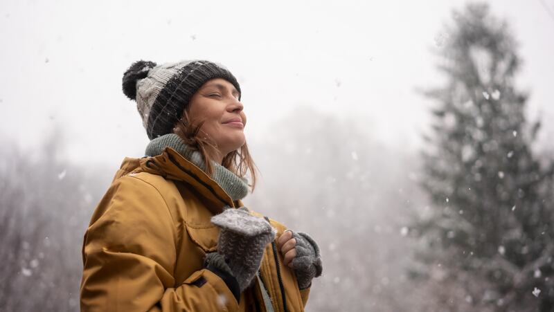 A young woman stands in a snowy forest wearing a hat and coat.