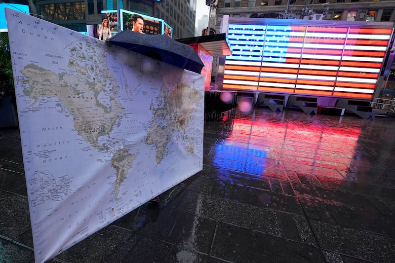 A pedestrian carrying a map of the world pauses in front of the Armed Forces Recruitment Center, Thursday, Oct. 29, 2020, in New York’s, Times Square.