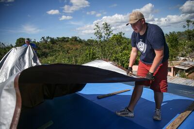 Al Dustin, left, and Statton Davis, 17, right, lay a new tarp on the leaking roof at Aida Valentine's home in Furnias Barrio, Puerto Rico, on Sunday, Dec. 10, 2017.