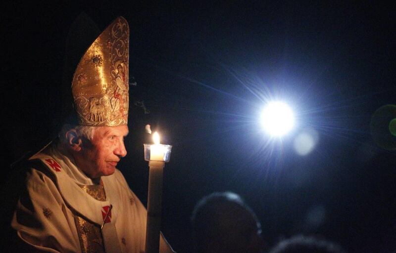 Pope Benedict XVI, holding a tall, lit, white candle, enters a hushed and darkened St. Peter's Basilica, at the Vatican Saturday, April 7, 2012, to begin the Vatican's Easter vigil service.