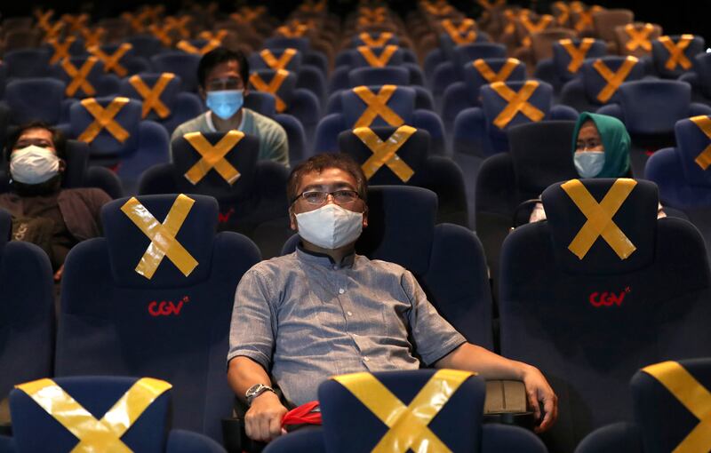 People sit spaced apart amid physical distancing markers as they wait for the start of a movie at CGV Cinemas theater in Jakarta, Indonesia, Friday, Oct. 23, 2020. The cinema reopened this week after months of closure due to coronavirus outbreak.