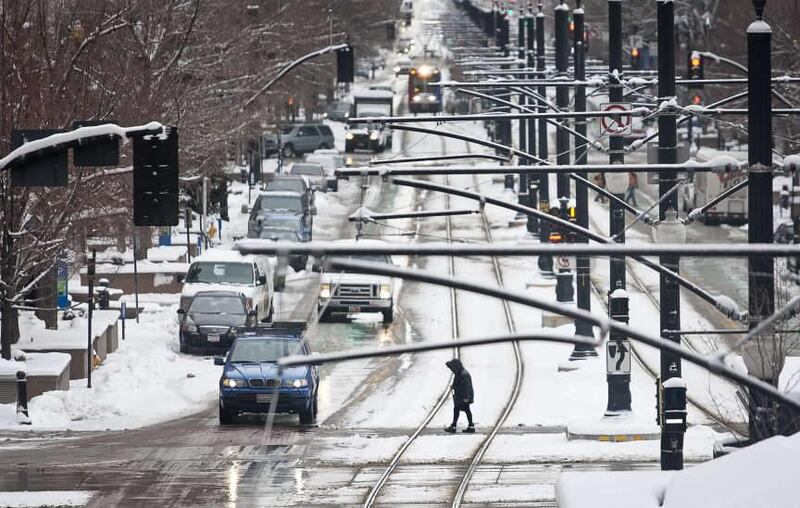 A pedestrian walks along the crosswalk at the intersection of 200 S. and Main Street in Downtown Salt Lake City as snow falls, Friday, Dec. 28, 2012.