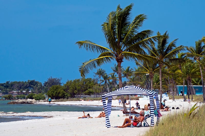 In this photo provided by the Florida Keys News Bureau, residents in Key West, Fla., get their first taste of sun and sand on the subtropical island, Tuesday, April 28, 2020, since city beaches were closed March 17, 2020, due to coronavirus concerns. On Monday, April 27, city officials began to relax some public recreation restrictions, including reopening city beaches. Key West and other regions of the Florida Keys remain closed to visitors. (Rob O’Neal/Florida Keys News Bureau via AP)