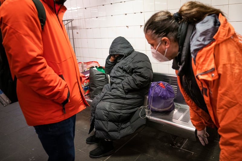 Homeless Outreach personnel reach out to a person sleeping on a bench in the Manhattan subway system.