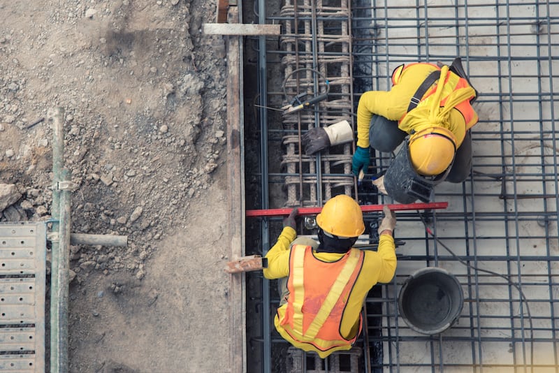 An arial view of two construction workers building the foundation of a building with interweaving wires.