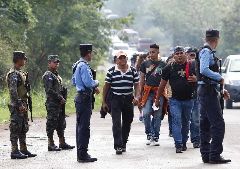 U.S.-bound migrants walk past security forces who are stopping some vehicles carrying migrants to check their documents in Cofradia, Honduras, early Tuesday, Jan. 15, 2019. Yet another caravan of Central American migrants set out overnight from Honduras,