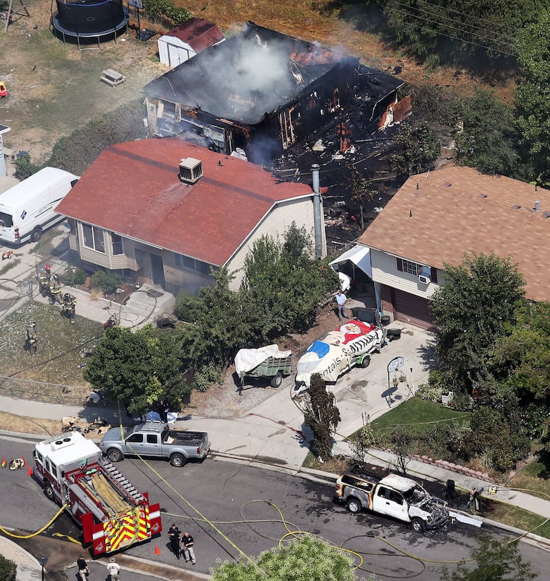 The charred remains of a building (top), a body covered by a sheet (behind the silver truck, front left) and a burned-out West Valley code enforcement truck (front right) are pictured at the scene of a fire and fatal shooting in West Valley City on Thursd