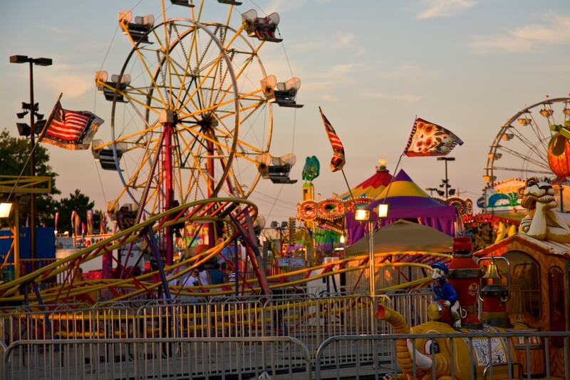 A fair is shown with a ferris wheel and other rides.