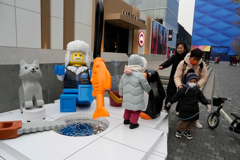 Children play near a display depicting an elderly person at a shopping mall in Beijing, Wednesday, Jan. 17, 2024.