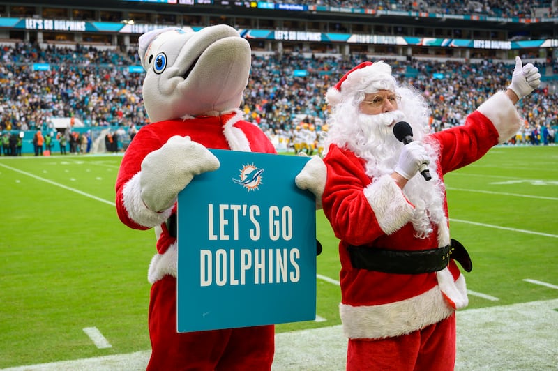 Miami Dolphins mascot T.D., wearing a Santa jacket and sign, helps Santa cheer on the fans before an NFL football game.