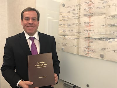 Elder Eduardo Gavarret holds a book with his family history while standing next to a large poster showing his family tree.