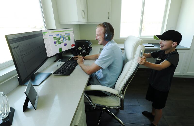 Tyson Oldham works in his home office as his son Carson rattles his chair.