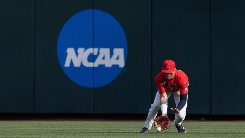 A college baseball player fields a ball with the NCAA logo behind him.