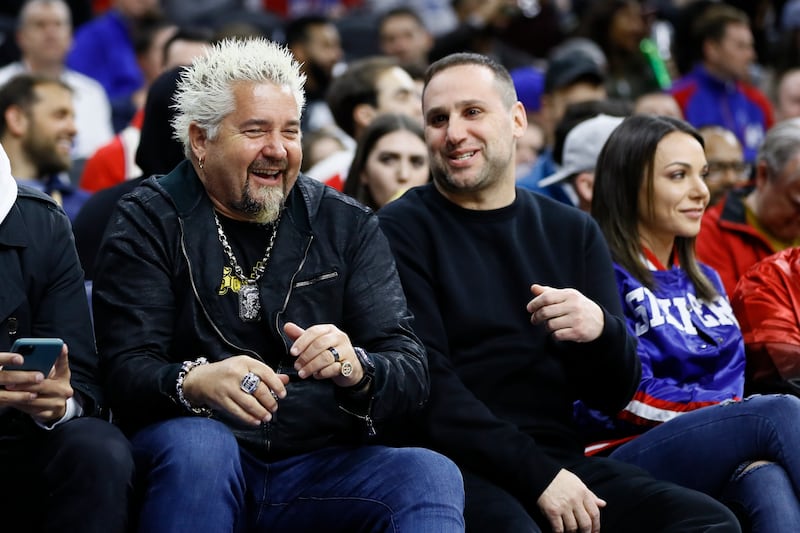 Restauranteur Guy Fieri, left, and Philadelphia 76ers’ Michael Rubin laugh during an NBA basketball game between the Philadelphia 76ers and the Detroit Pistons, Wednesday, March 11, 2020, in Philadelphia. (AP Photo/Matt Slocum)