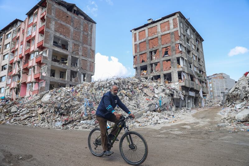 A man rides a bicycle past destroyed buildings in Antakya, southeastern Turkey, Tuesday, Feb. 21, 2023. The death toll in Turkey and Syria rose to eight in a new and powerful earthquake that struck two weeks after a devastating temblor killed nearly 45,000 people, authorities and media said Tuesday.