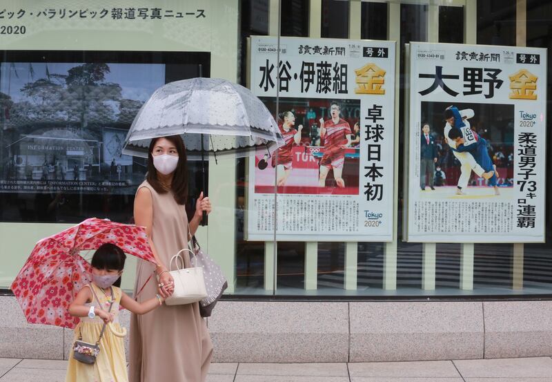 People wearing face masks walk past extra papers reporting on Japanese gold medalists at Tokyo Olympics.